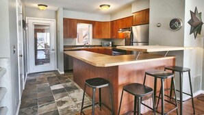A kitchen with wooden cabinets, a stainless steel refrigerator, a microwave, and a bar area with stools. - GREAT OLD TOWN LOCATION- SKI TO TOWN LIFT & STEPS TO MAIN ST!  (Park City)