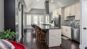 A modern kitchen with a central island, stainless steel appliances, and a brick accent wall. -  Luxe Three floors. Four bedrooms each with private full bath  Garage Parking (Washington)