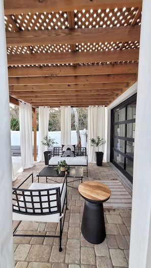 Um pátio externo com pérgola de madeira, área de estar e plantas em vasos.