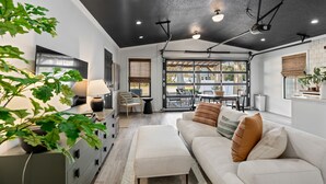 Ein modernes Wohnzimmer mit einem weißen Sofa, einem Couchtisch und einem Essbereich mit Tisch und Stühlen. Ein großes Fenster sorgt für natürliches Licht und einen Ausblick ins Freie.