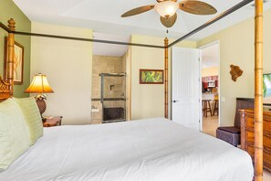 Une chambre avec un grand lit, un ventilateur de plafond, une douche et une vue sur la cuisine.