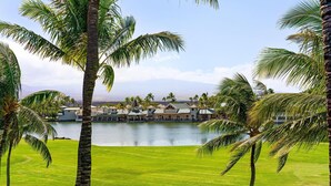 Ein Golfplatz mit einem See, Palmen und einem Gebäudekomplex im Hintergrund.