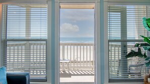 A room with a view of the beach through open French doors, a blue sofa, and a potted plant. - Stunning Beachfront Condo - Recently Remodeled! (Galveston)