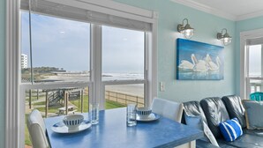 A dining area with a table and chairs, a view of the beach, and a painting of swans on the wall. - Stunning Beachfront Condo - Recently Remodeled! (Galveston)