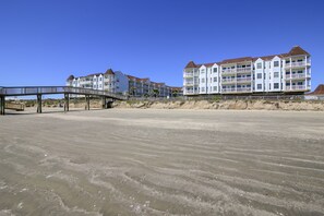 Um hotel à beira-mar com várias varandas, um calçadão de madeira e uma praia arenosa.