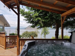 A wooden deck with a hot tub, overlooking a lake with trees and mountains in the background. - Sat-Sat Summer Water Trampoline, HotTub, Canoe,Paddle Boards,Kayaks, Dock/Buoy
 (Blind Bay)