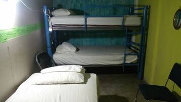 Una camera con un letto a castello, un letto singolo in basso e due letti a castello sopra. C'è una sedia e un piccolo tavolo con una lampada.