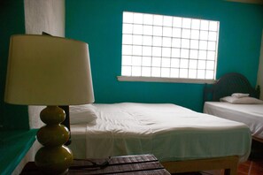 Une chambre avec deux lits, une fenêtre à carreaux et une lampe sur une table.