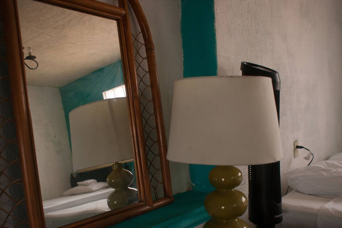 Een hotelkamer met een bed, een bedlamp, een spiegel en een wand in teal.
