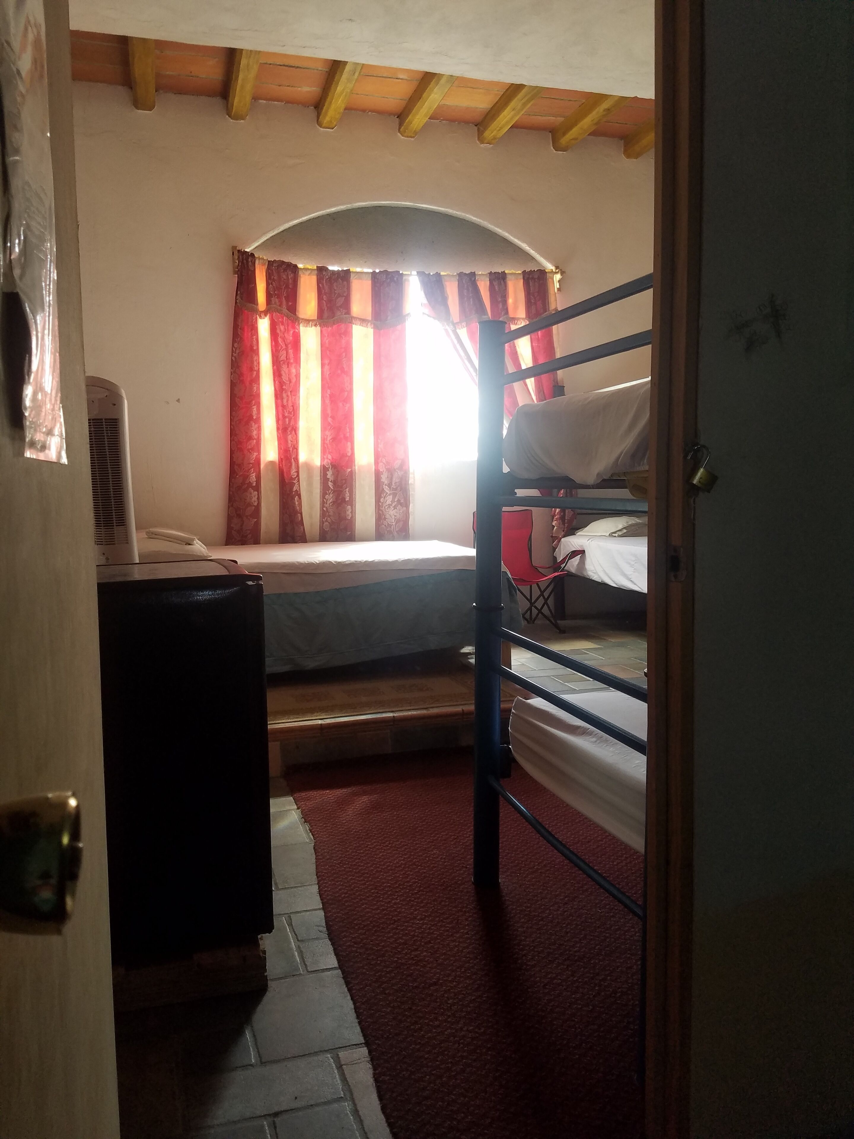 Ein Zimmer mit Etagenbett, einem kleinen Schreibtisch mit Stuhl, einem roten Teppich und einem Fenster mit Vorhängen.