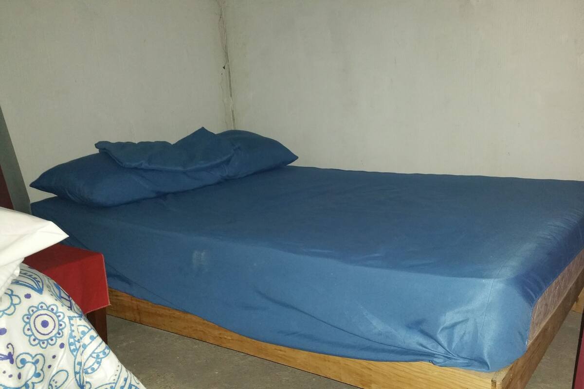 Een enkel bed met een blauwe matras en kussens, een houten frame en een witte muur.