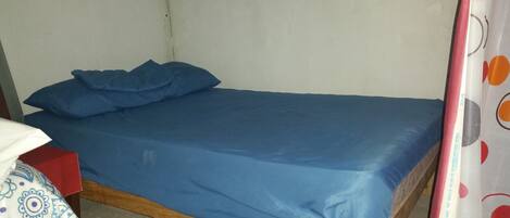 A single bed with a blue mattress and pillows, a wooden frame, and a white wall.