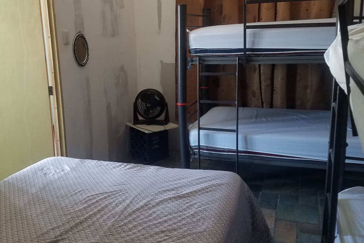 Een slaapzaal met stapelbedden, een ventilator en een deur.