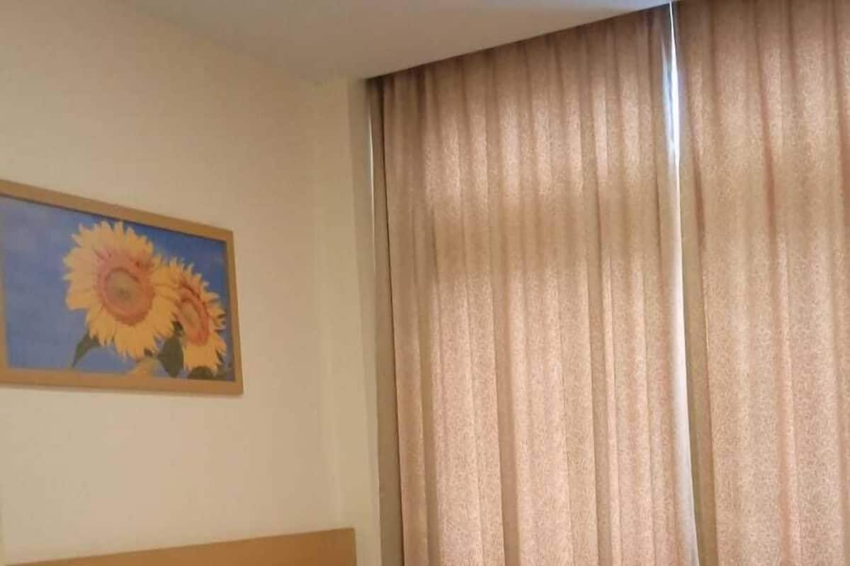 Hotellihuone, jossa on sänky, sängynpääty, auringonkukkamaalaus ja ikkuna, jossa on verhot.