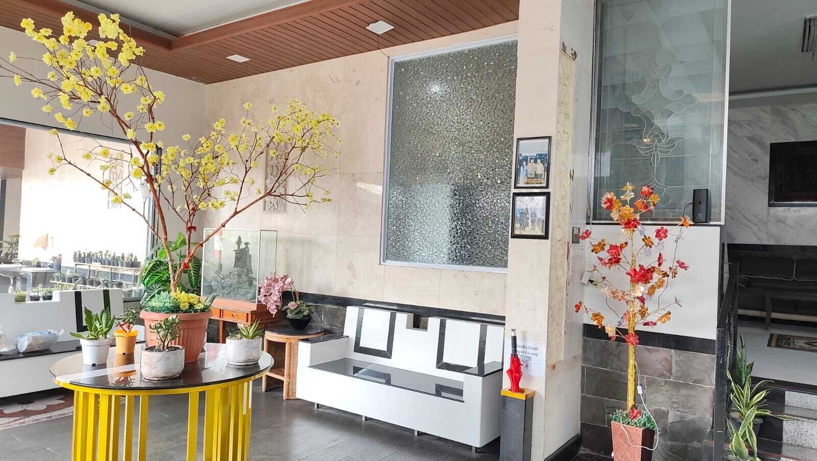 A hotel lobby with a reception desk, seating area, and decorative plants.