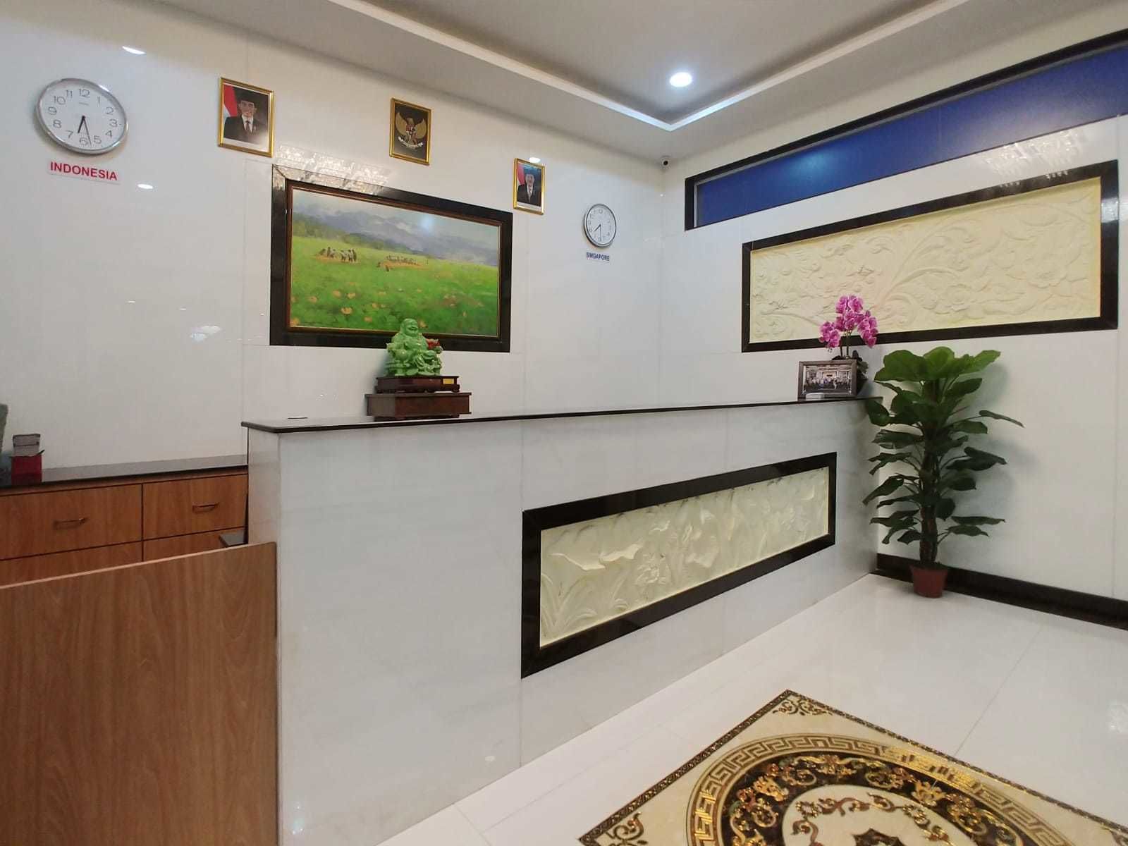 A reception area with a clock, framed pictures, a green statue, and a potted plant.