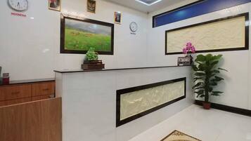 A reception area with a clock, framed pictures, a green statue, and a potted plant.