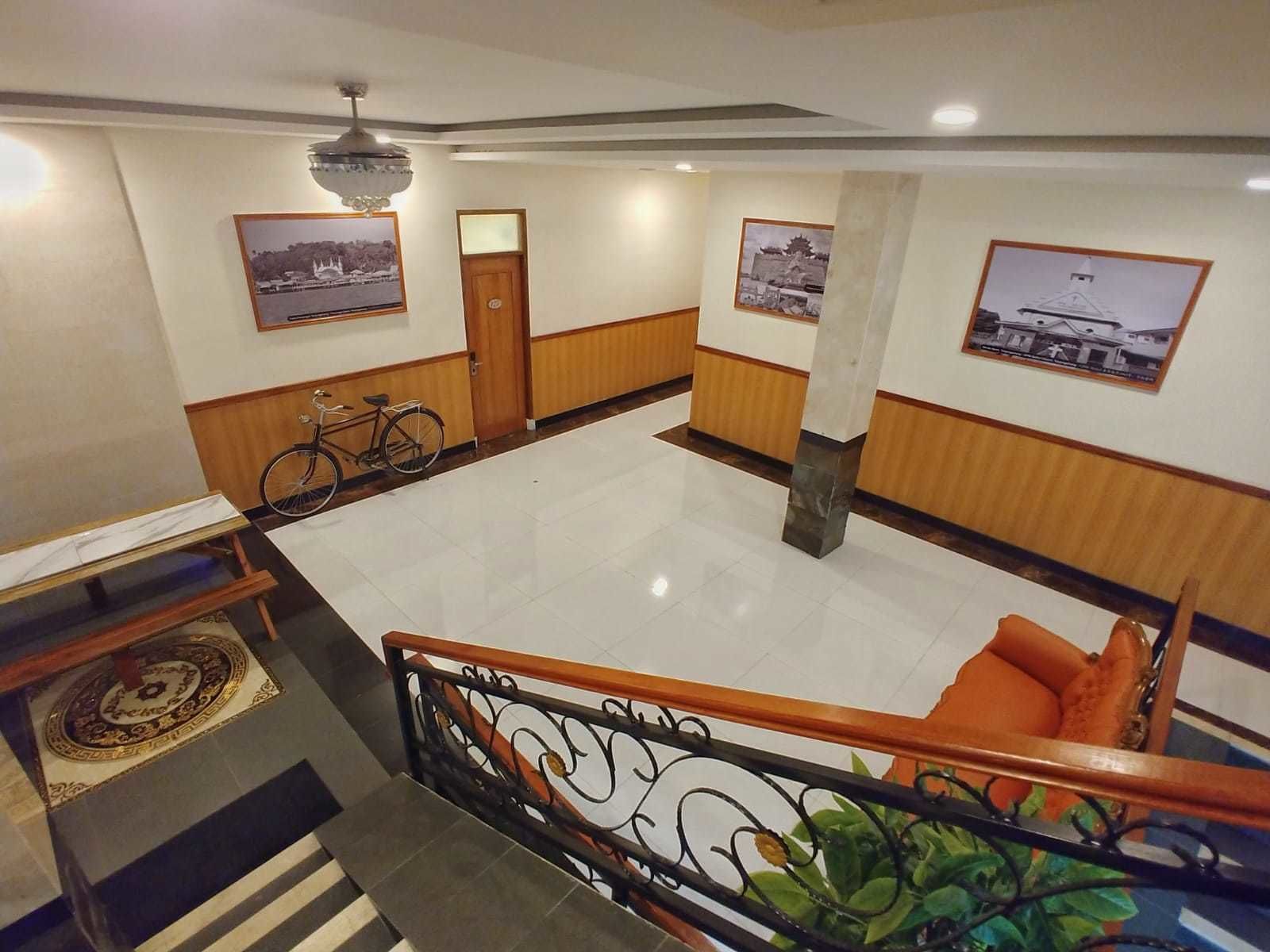A spacious lobby with a tiled floor, a wooden bench with orange cushions, a bicycle, and framed pictures on the walls.
