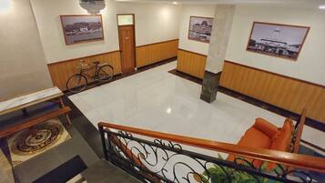 A spacious lobby with a tiled floor, a wooden bench with orange cushions, a bicycle, and framed pictures on the walls.