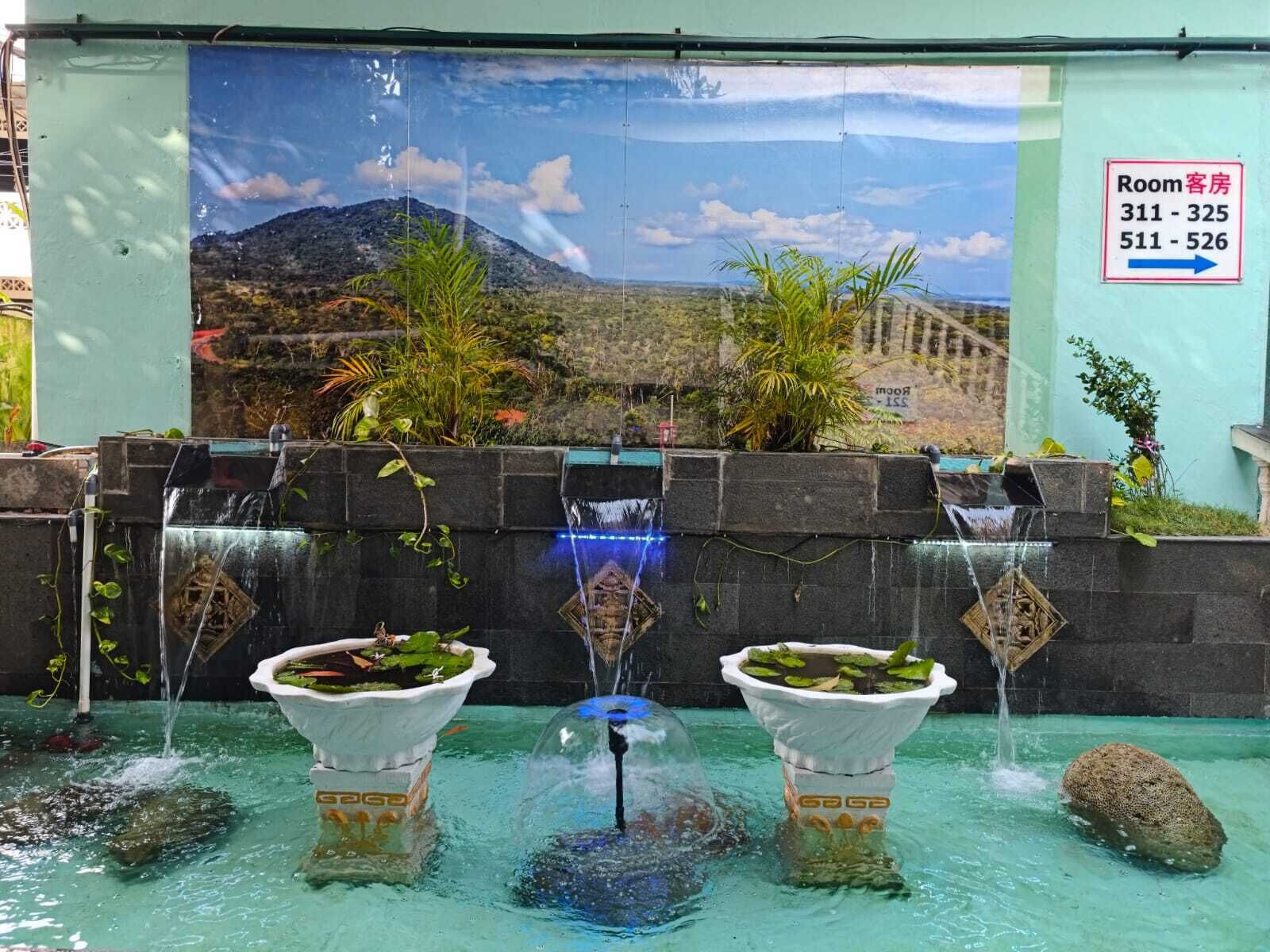 A pool area with multiple water features, including a waterfall and two water fountains, set against a backdrop of a mural depicting a mountainous landscape.