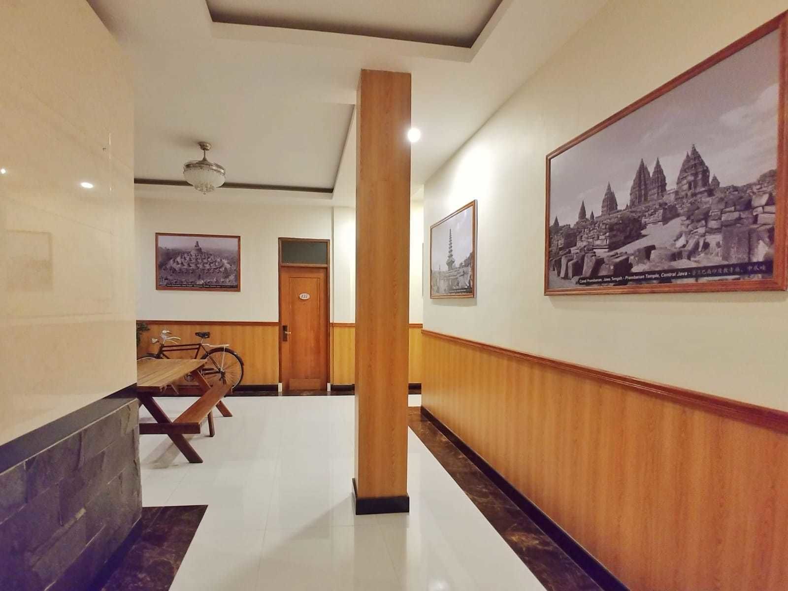 A hotel corridor with wooden paneling, a polished floor, and framed pictures of temples.