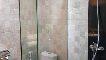 A glass-enclosed shower stall with a toilet inside, tiled walls, and a handheld showerhead.