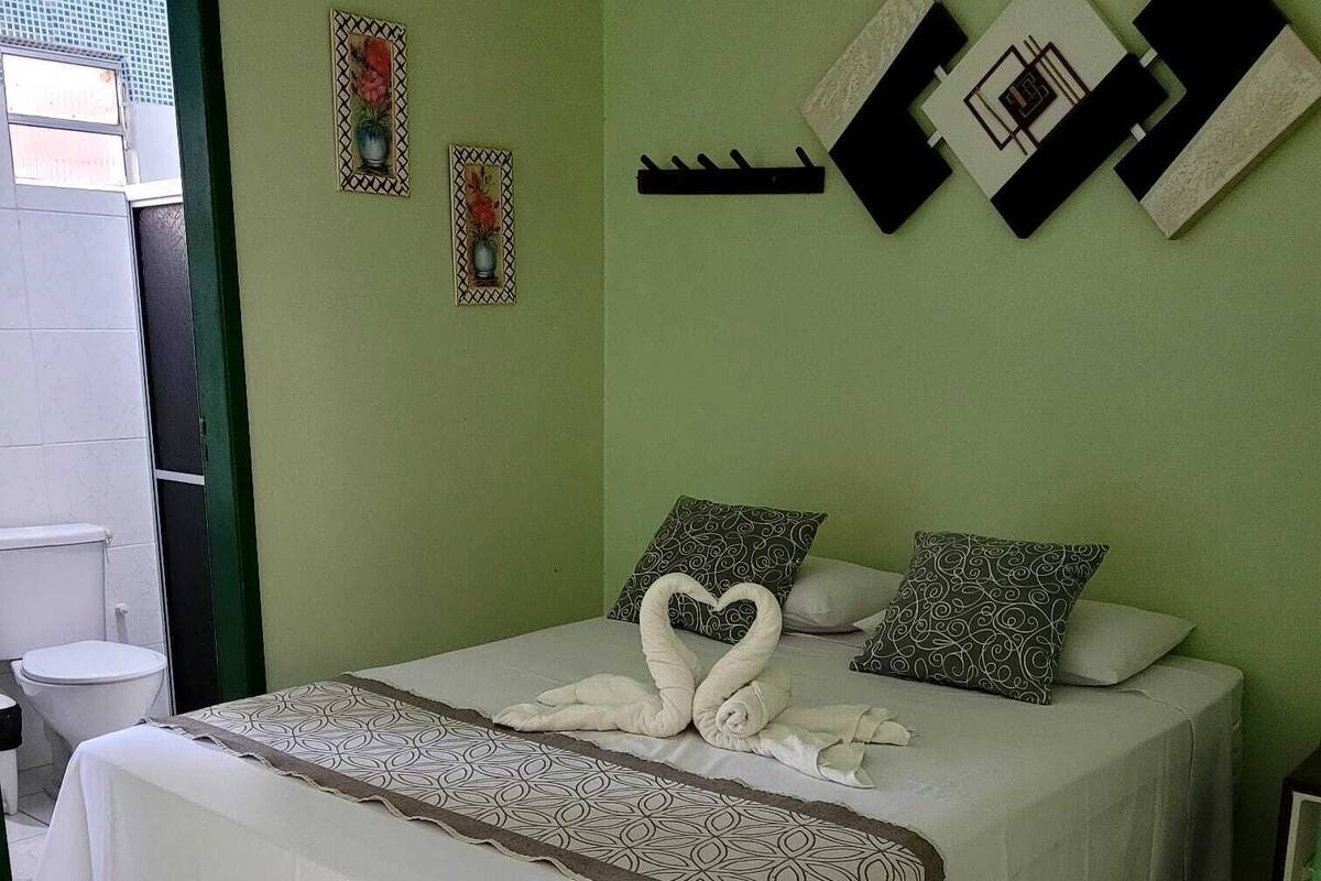 Una cama impecable con una toalla dispuesta en forma de corazón, un plaid estampado y cojines decorativos.
