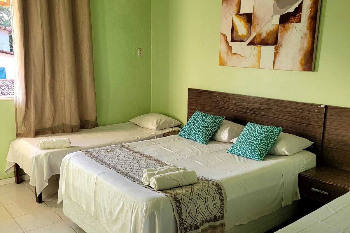 Una habitación con dos camas individuales, una cama grande con cubrecama estampado y un cuadro abstracto colgado en la pared.