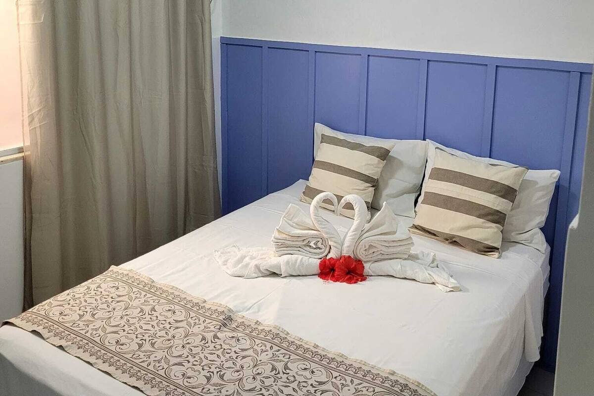 Una cama bien tendida con cabecera azul, ropa de cama blanca y almohadones decorativos.
