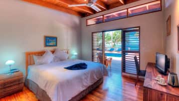 A bedroom with a bed, a desk with a computer, a TV, and a view of an outdoor pool area.