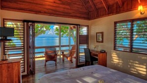 A bedroom with a bed, a desk, and a chair, with a view of the sea through large windows. - Beachfront Private Villa (Korolevu)