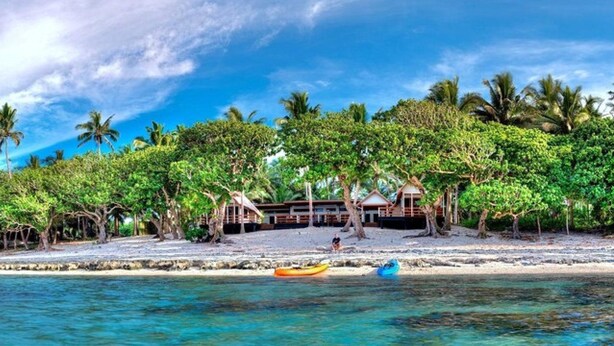 A beach resort with a thatched-roof building surrounded by lush greenery and palm trees. - Beachfront Private Villa (Korolevu)