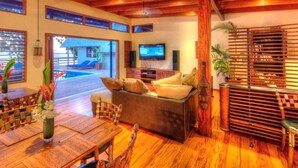 A spacious living area with a wooden floor, a sofa, a TV, and a view of an outdoor pool. - Beachfront Private Villa (Korolevu)