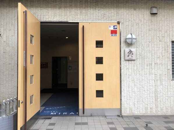 A hotel entrance with a wooden door, a welcome mat, and a security camera. - Hotel Mirai (Yokohama)