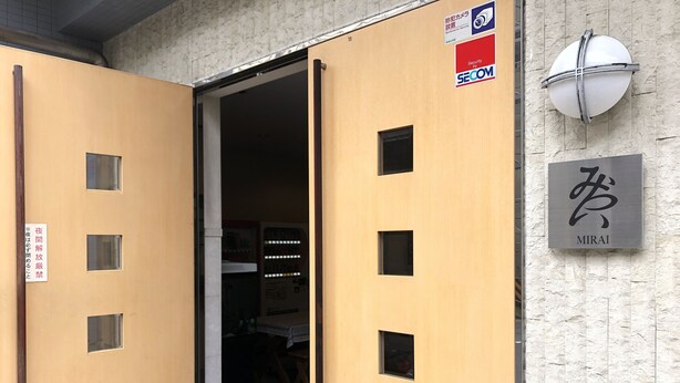 Entrada de un hotel con puerta de madera, cámara de seguridad y cartel que indica seguridad por SECOM.