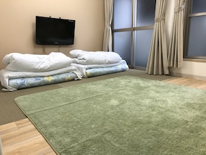 A room with a green carpet, a bed with white bedding, a television on the wall, and a window with curtains. - Hotel Mirai (Yokohama)