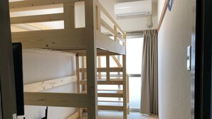 Una habitación con literas, suelo de esterilla de tatami, ventilador de techo y ventana con cortinas.