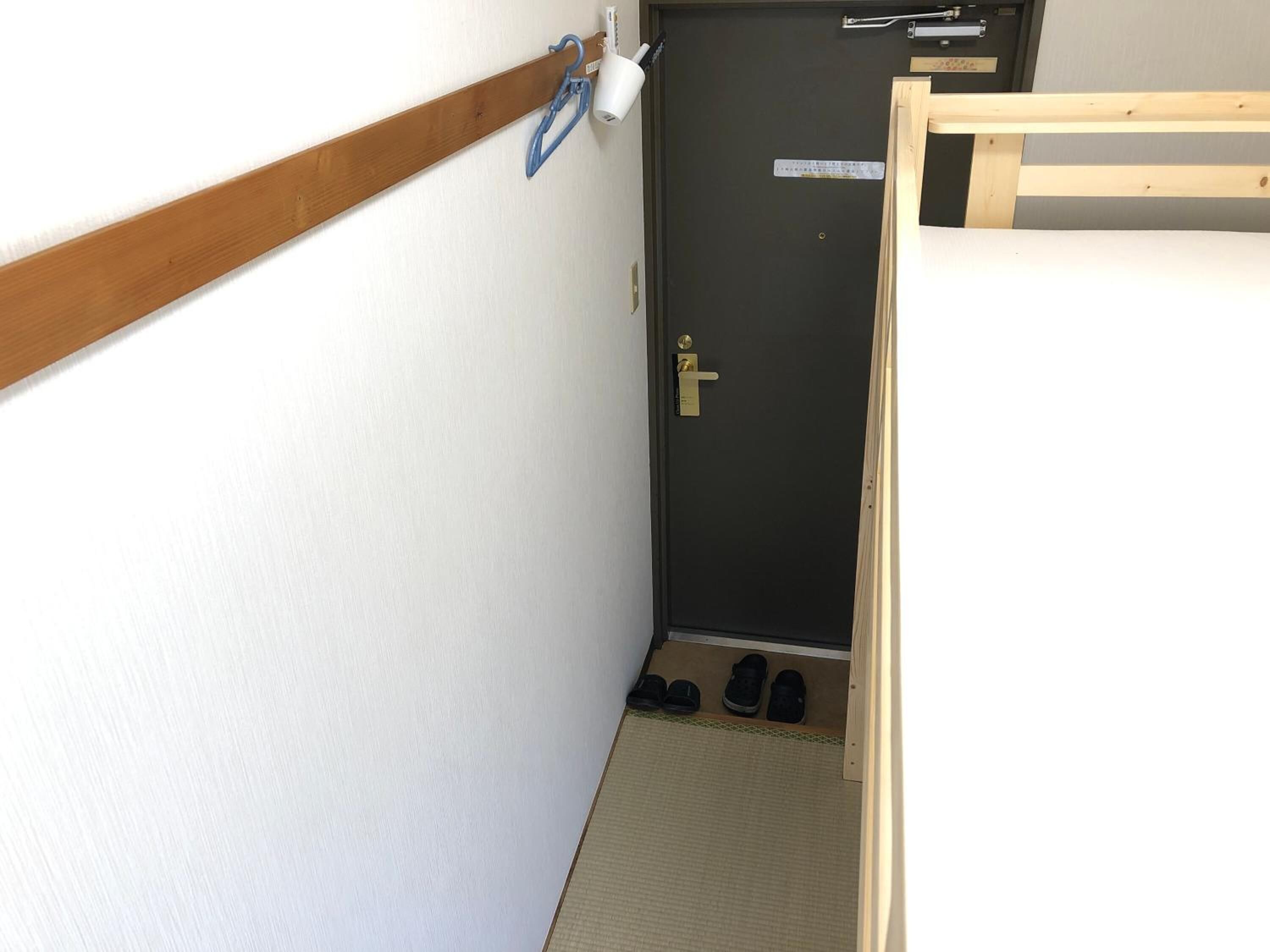 A narrow hallway with a wooden bench on the right, a door with a doorknob, and a small shoe rack with shoes.