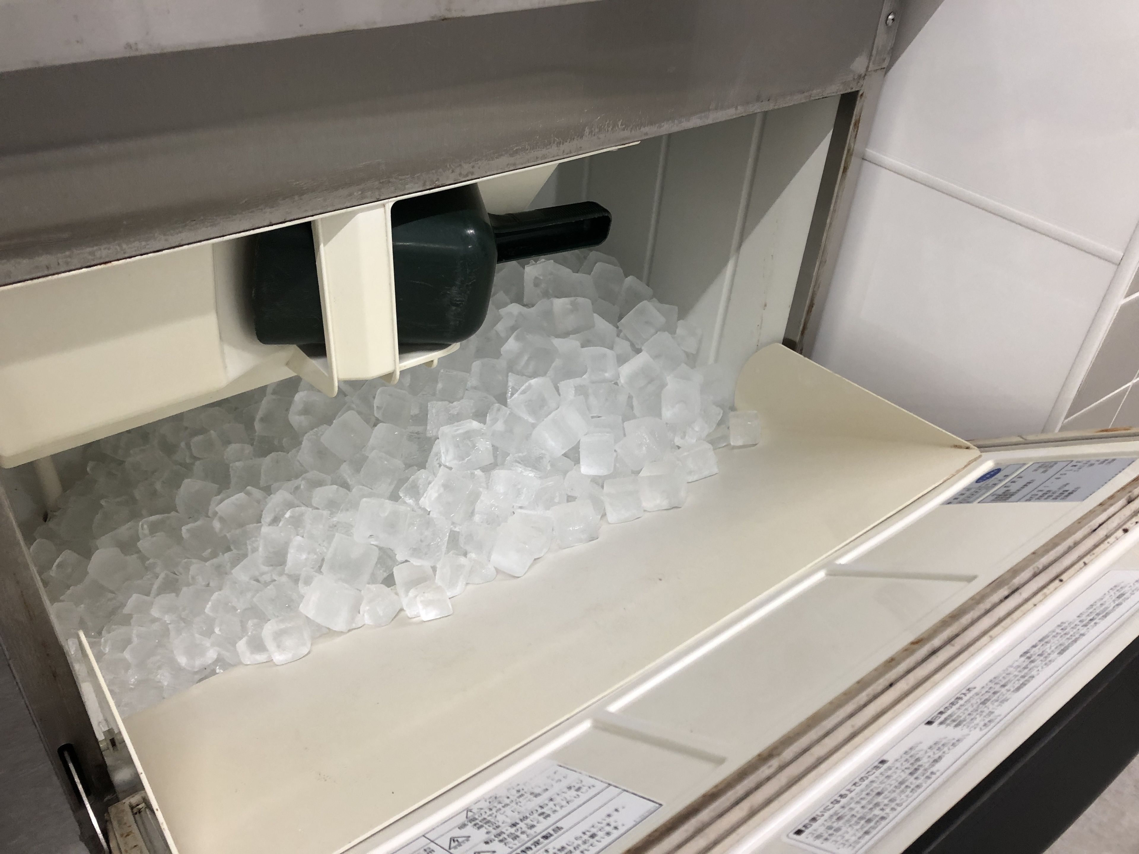 A storage area with a container filled with ice cubes and a black object, possibly a tool, on a shelf.