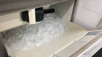 A storage area with a container filled with ice cubes and a black object, possibly a tool, on a shelf.