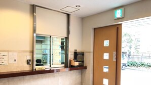 Un área de recepción con un escaparate de vidrio, un mostrador con computadora y una puerta con letrero de salida de emergencia.