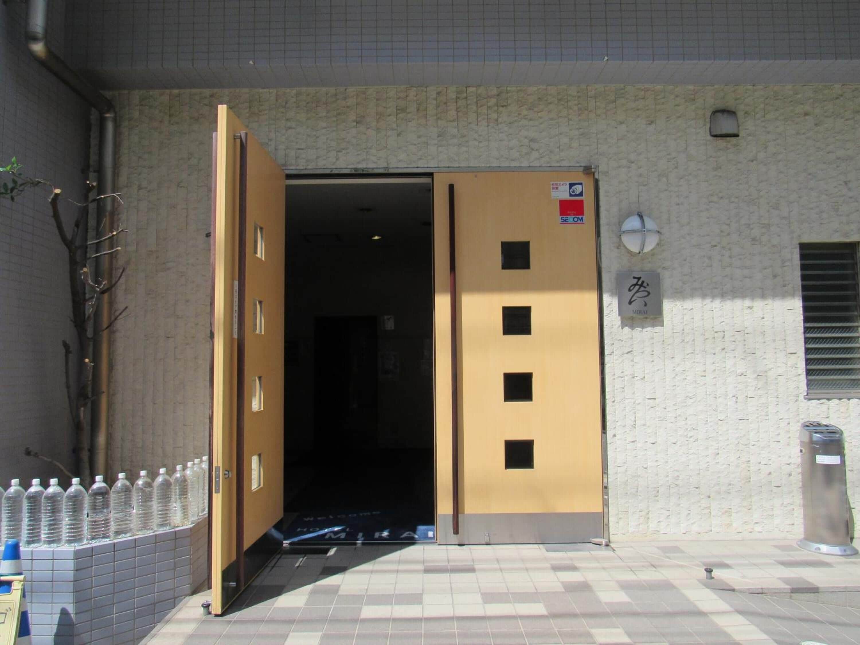 L’entrée d’un hôtel, avec un sol carrelé, une porte en bois et une enseigne indiquant le nom de l’hôtel.