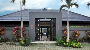 A modern building with a dark roof and a central entrance flanked by two palm trees. - Modern Family Villa (Kerobokan)