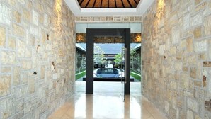 A stone-walled hallway leading to a glass door with a view of a garden and a building outside. - Modern Family Villa (Kerobokan)