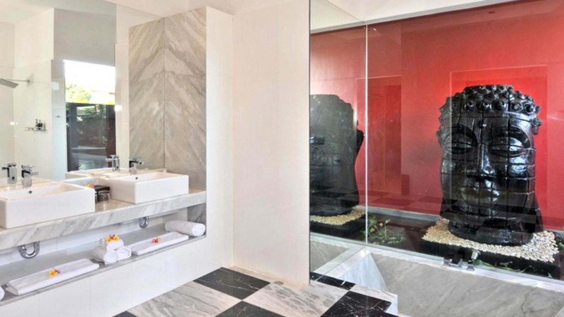 Een moderne badkamer met een grote spiegel, twee wasbakken en een decoratief Boeddhabeeld achter glas.
