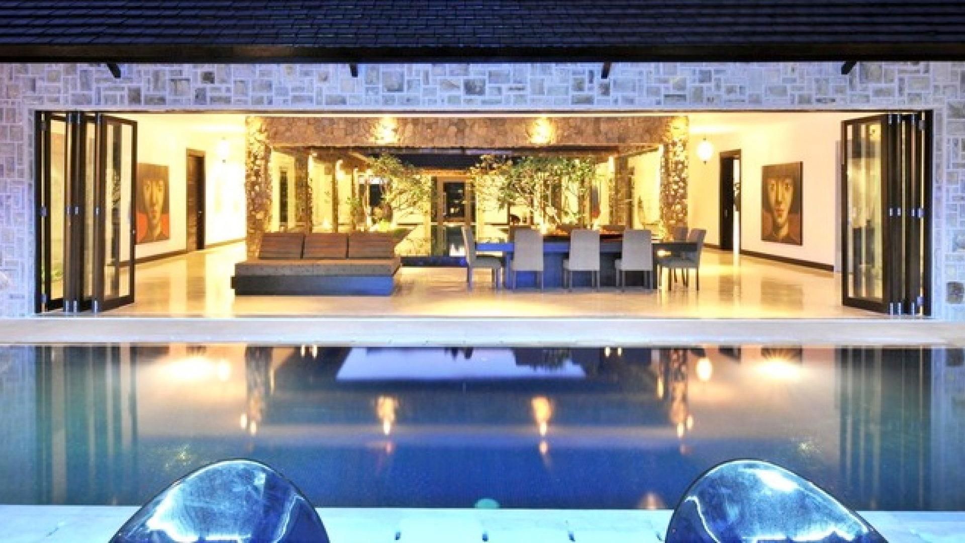A modern indoor pool area with a glass barrier, seating, and a stone wall backdrop.