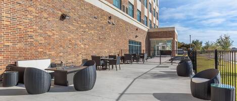 An outdoor patio with seating and tables, a brick building, and a clear sky.