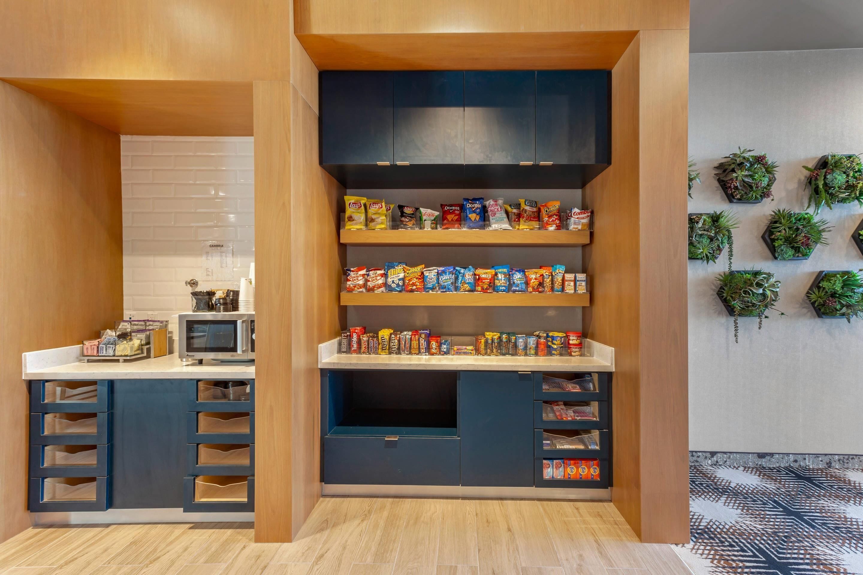A kitchen with wooden cabinets, a microwave, and shelves stocked with snacks.