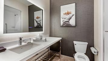 Un baño moderno con lavamanos, espejo y retrete blancos.