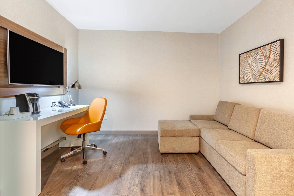 A modern room with a white desk, orange office chair, and a beige sectional sofa.